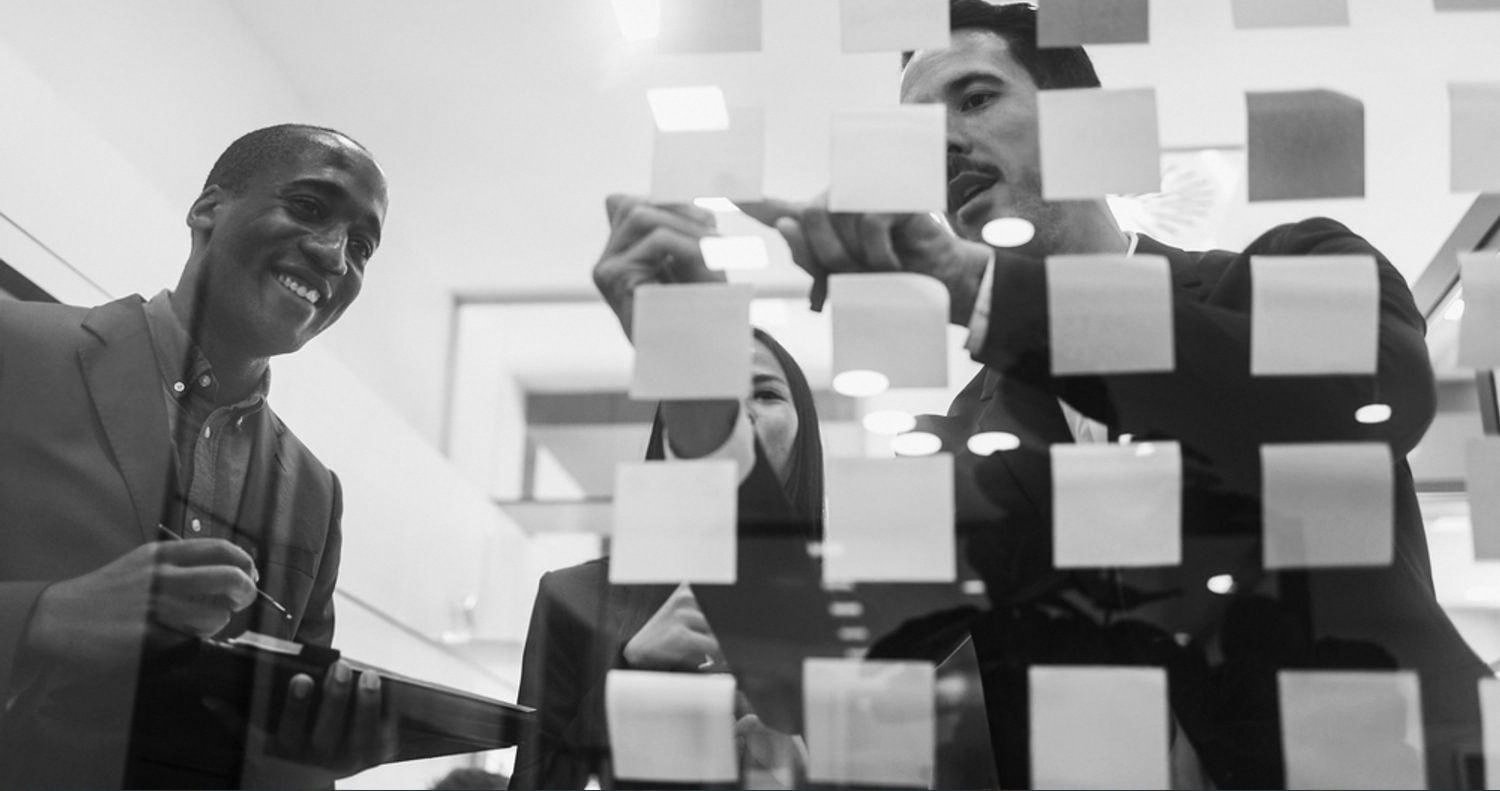 Managers mapping out a change plan on a glass wall covered in sticky notes